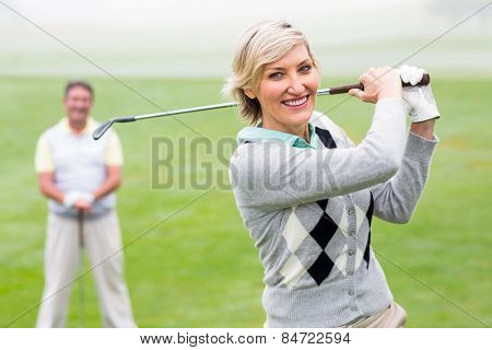 Lady golfer teeing off for the day watched by partner on a foggy day at the golf course