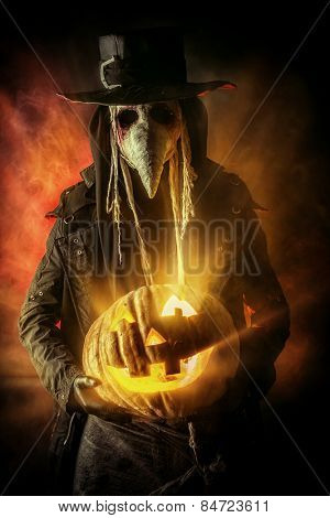 Frightening plague doctor stands with a pumpkin. Medieval Europe. Halloween.