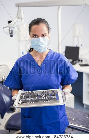 Portrait of a dentist with surgical mask and holding tray in dental clinic