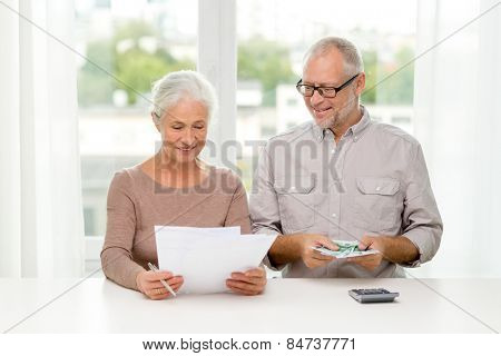 family, savings, age and people concept - smiling senior couple with papers, money and calculator at home
