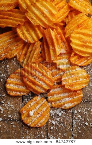 Delicious potato chips with salt on wooden table close-up