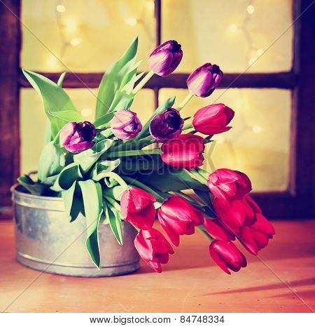 tulips on a wooden board in front of a window pane with bokeh toned with a retro vintage instagram filter app 