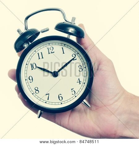closeup of the hand of a man holding a mechanical alarm clock, with a retro effect