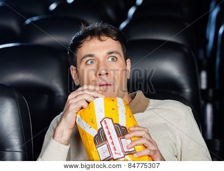 Frightened man eating popcorn while watching movie in cinema theater