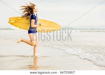 Beautiful sexy surfer girl on the beach at sunset running into ocean, yellow surfboard in her hands.