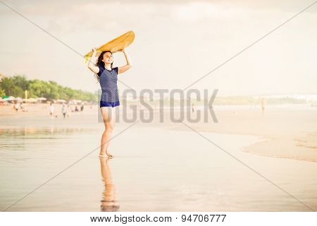Beautiful sexy surfer girl on the beach at sunset walks along ocean shore, yellow surfboard in her h