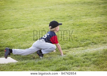 Young boy baseball player waiting on third base. He showing a funny sprinters stance