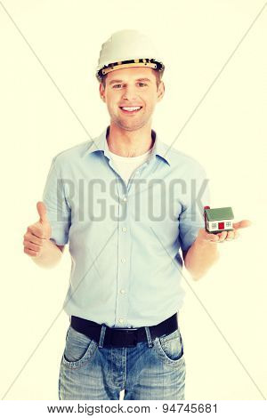 A forewoman holding a model house in hand and gesturing OK
