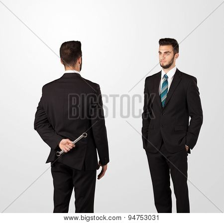 Two opposing businessman shake hands, one of them hiding a weapon behind his back