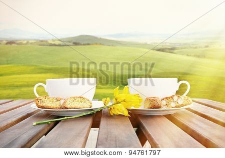 Coffee and cantuccini on the wooden table against Tuscan landscape. Italy