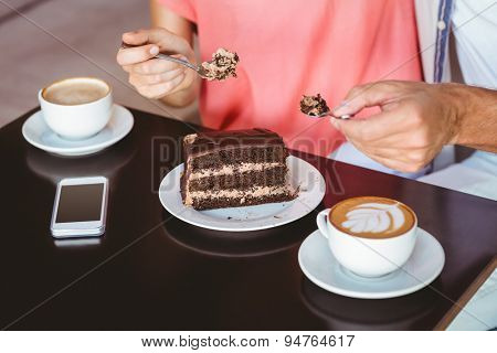 Cute couple on a date sharing a piece of chocolate cake at the cafe