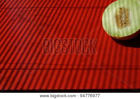 Background with halfs of sugar melon, red tabletop and stripped effect of sunblind.