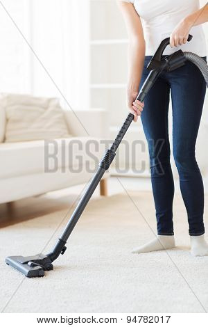 people, housework and housekeeping concept - close up of woman with vacuum cleaner cleaning carpet at home