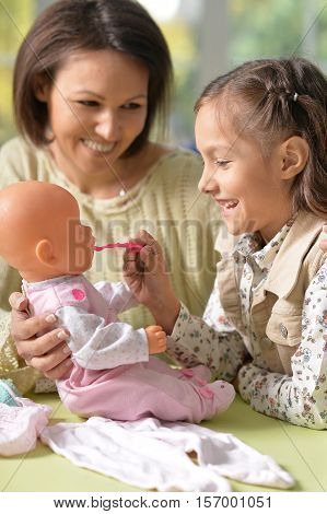 Portrait of happy mother and her cute daughter play with baby doll together