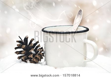 Old mug with a hot drink and with a fir-cone on a wooden stump in the snow in the outdoors. Photo in vintage color image style. Coffee break outdoors. Morning Still life. Morning at the campsite.
