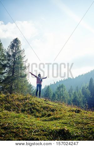 Mid low angle shot of positive woman who is spreading hands and feeling the freedom on the mountain peak on a fair day. Stunning vista of the mountain valley covered with majestic forests 