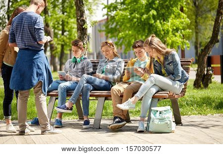 education, high school and people concept - group of happy teenage students with tablet pc computers sitting on bench at campus yard