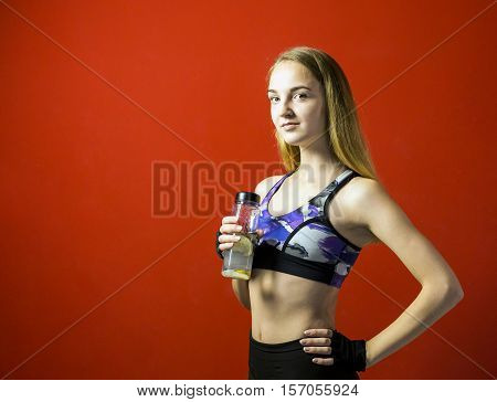 Young attractive blonde fitness girl wear in sport top holding sport bottle, smiling to camera on red