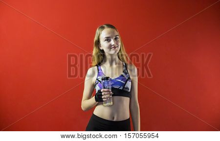 Young attractive blonde fitness girl wear in sport top holding sport bottle, smiling to camera on red