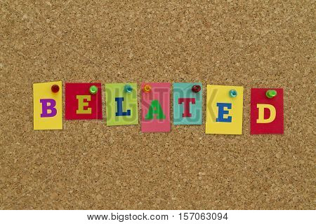 Belated word written on colorful sticky notes pinned on cork board.