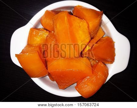Slices of pumpkin with sugar baked in the oven. The white plate on a black background