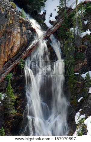 Yellowstone National Park steel foot canyon bridge resisting heavy waterfall from snow melt.