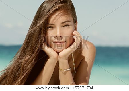 Beautiful portrait of young brunette mixed race Asian Caucasian woman on beach with sepia filter for a vintage look. Serene looking model with healthy brown hair relaxing on beach on vacation travel.