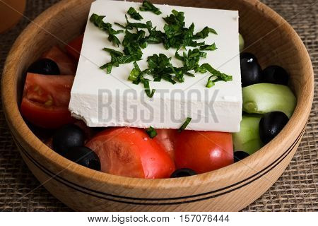 Greek salad with feta cheese and vegetables on wooden plate