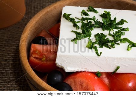 Greek salad with feta cheese and vegetables on wooden plate