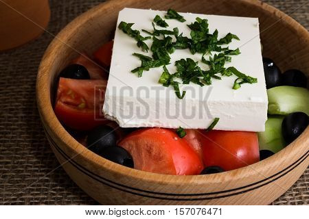 Greek salad with feta cheese and vegetables on wooden plate