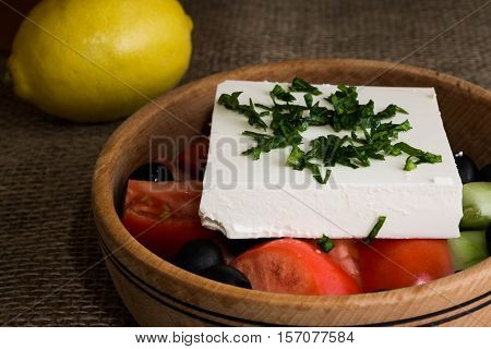 Greek salad with feta cheese and vegetables on wooden plate