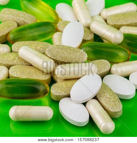 Mixed natural food supplement pills omega 3 calcium multivitamin and glucosamine capsules on green background