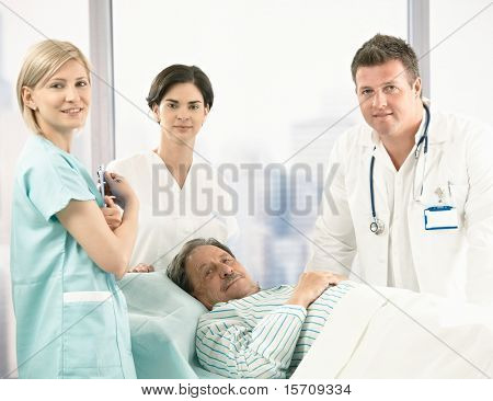 Retrato de sênior paciente deitado na cama, rodeada com tripulação de hospital, sorrindo para a câmera.?
