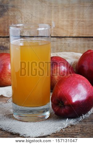 Glass of apple juice and red apples on old wooden background