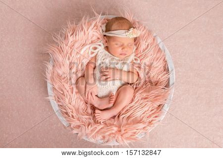 sweet newborn girl in white romper sleeping on round cot with fluffy blanket, top view