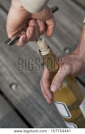 hand opening a wine bottle with a corkscrew. A man uncorking a bottle of white wine