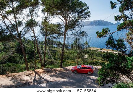 Alcudia Mallorca Spain - May 23 2016: Seascape of Mediterranean Sea with a red car Volvo V40 traveling on the mountain serpentine through the pine forest along the coast of Majorca. Auto travel concept