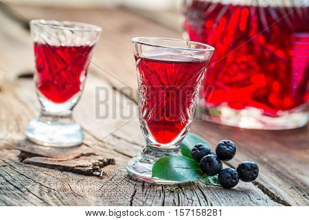 Homemade Liqueur With Chokeberries And Alcohol On Old Wooden Table