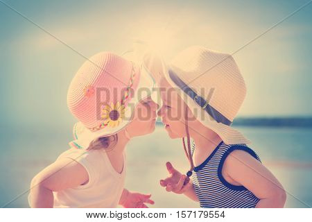 Babygirl and babyboy kissing on the beach in straw hats