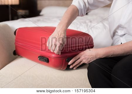 Red valise. Modern big red valise lying on the couch and aged woman touching it
