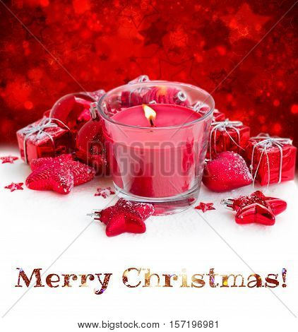 christmas red burning candle with christmas decorations on snow, red background with stras and mery christmas greetings
