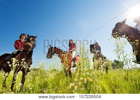 Portrait of happy equestrians riding bay horses in the flowery meadow at sunny day
