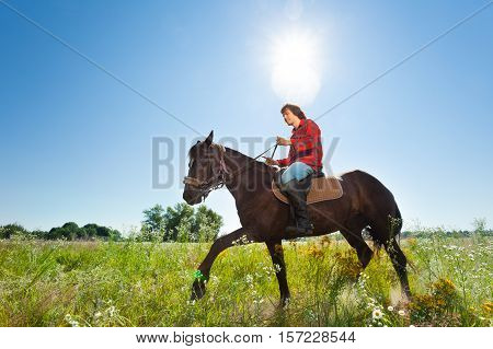 Side view portrait of young man horse ridding in the green outback in summer
