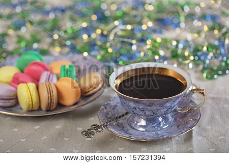 Colourful tasty macaroons and cup of coffee in xmas lights