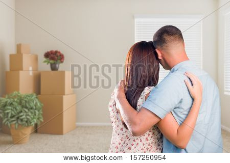 Young Military Couple Facing Empty Room with Packed Moving and Potted Plants.