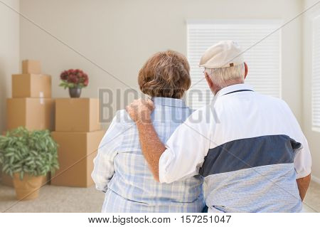 Senior Couple Facing Empty Room with Packed Moving Boxes and Potted Plants.