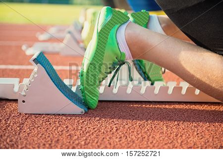 Feet on starting block ready for a spring start. Focus on leg of a athlete about to start a race in stadium with sun flare.