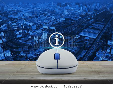Wireless computer mouse with information sign icon on wooden table over city tower street and expressway