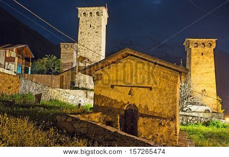 The tiny chapel on the old cemetery with the brightly illuminated Svan towers on the background Mestia Upper Svaneti Georgia.
