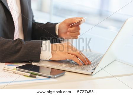 Businessman doing online banking making a payment or purchasing goods on the internet entering his credit card details on a laptop close up view of his hands